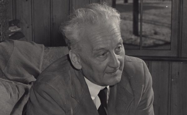 Albert sits on a chair, leaning forward with his elbows on his legs and hands clasped.
