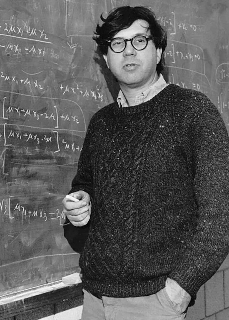 Black and white photo of man standing by a blackboard