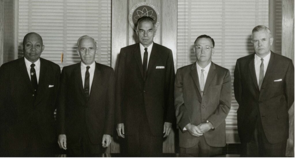 5 men wearing suits and ties standing shoulder to should. Seaborg is standing in the middle.