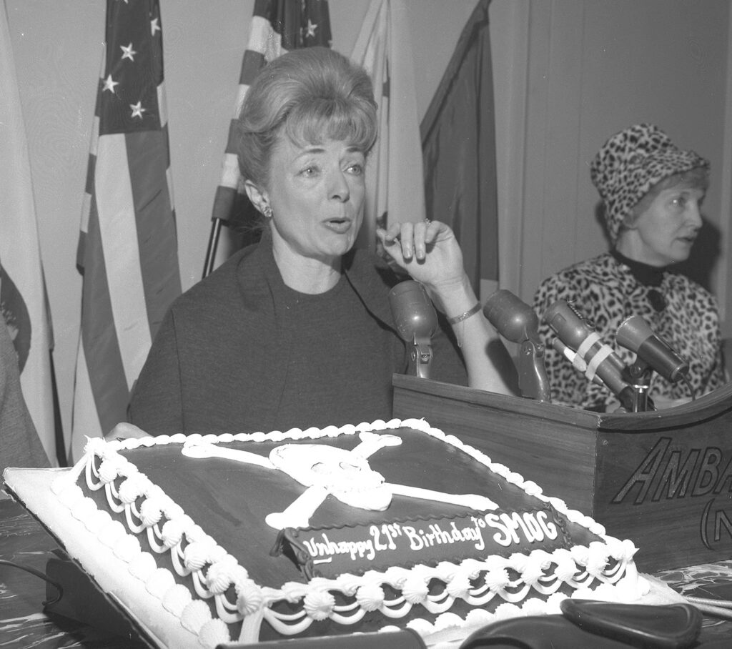 Woman seated in front of microphones with a decorated cake on display