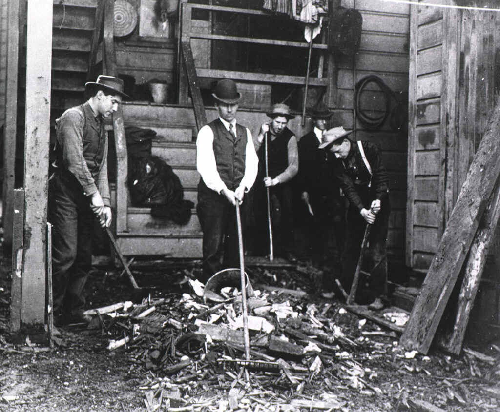 Group of men working with rakes and shovels in a cluttered backyard