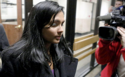 Photo of woman exiting building surrounded by news cameras