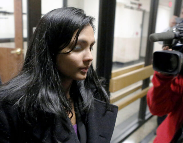 Photo of woman exiting building surrounded by news cameras