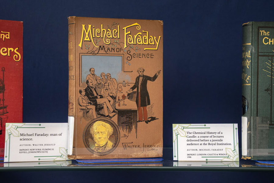 Michael Faraday: Man of Science book cover depicting a man in a black jacket and red pants presenting to a group of men and boys seated.