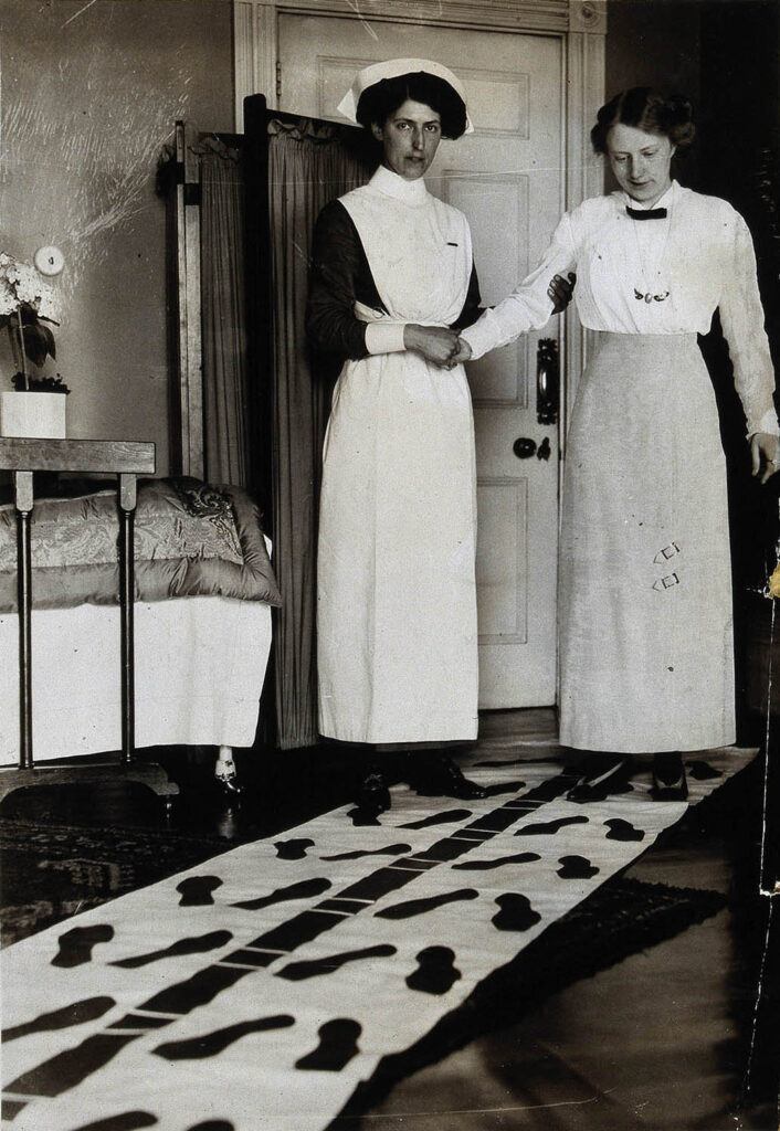 A nurse steadies a patient during physical therapy, undated.