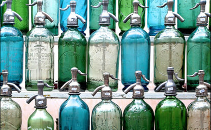 Photo of a shelf display of vintage soda bottles. Some bottles are clear, while others are tinted green or blue.