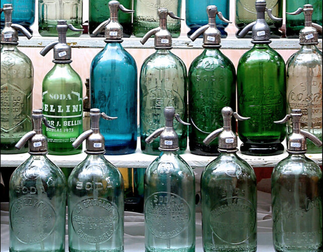 Photo of a shelf display of vintage soda bottles. Some bottles are clear, while others are tinted green or blue.