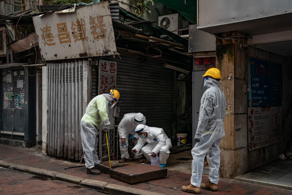 Workers in hazmat suits working around a manhole in a city street