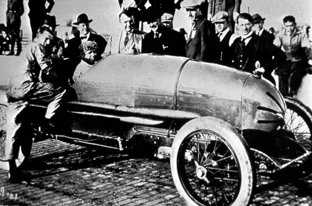 Black and white photograph of men surrounding a race car