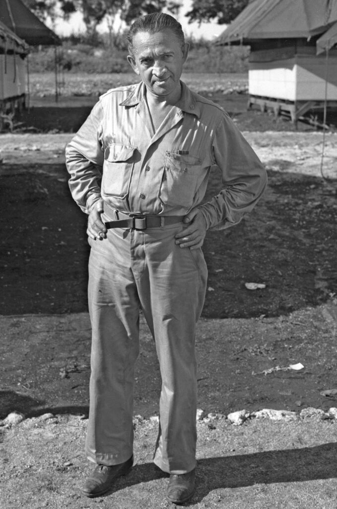 Laurence in military dress standing in temporary camp