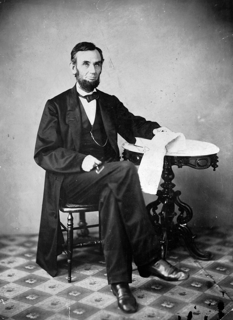 Black and white photograph of tall bearded man seated at small table