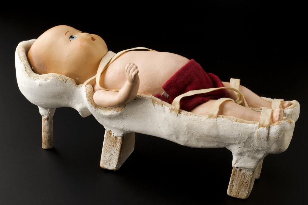 A small doll lies in stirrups on a faux hospital bed