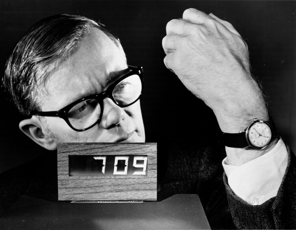 Man in glasses with showing wristwatch next to LCD clcok