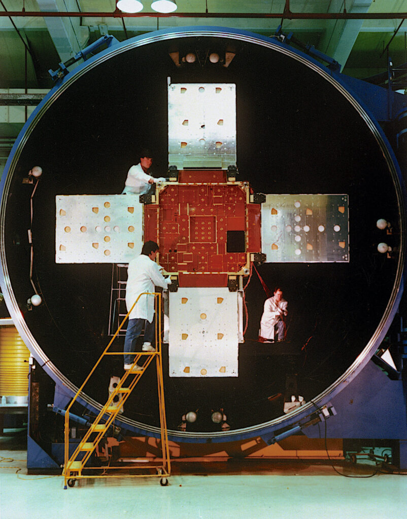 Three people in lab coats working on a satellite