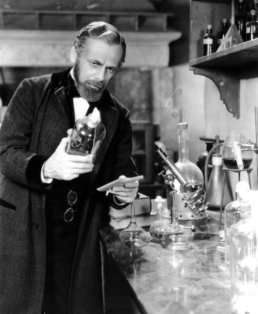 Black and white theatrical photo of man posing with glassware
