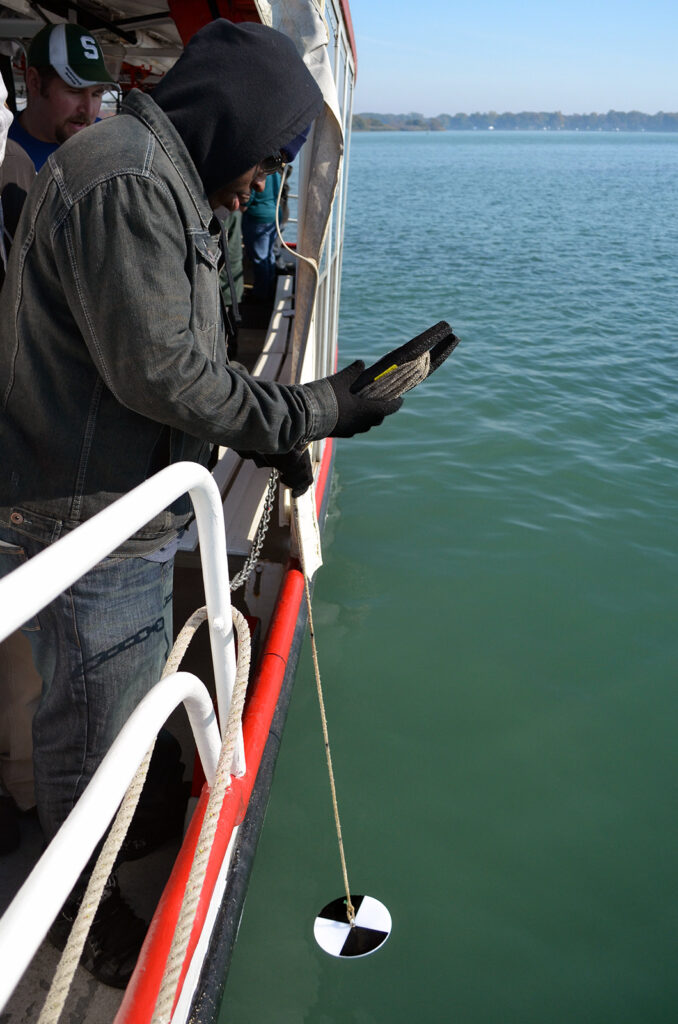 Photo of young man on a boat lowering a device into water
