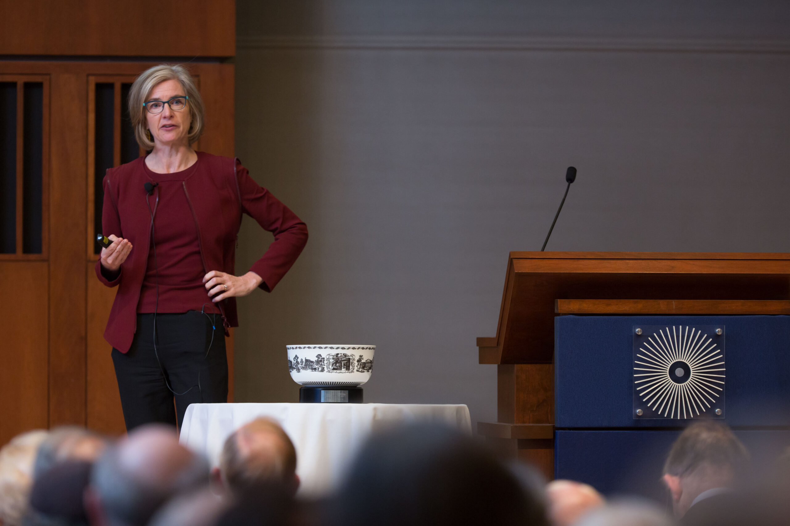 Woman in glasses standing beside lectern with a bowl in the foreground