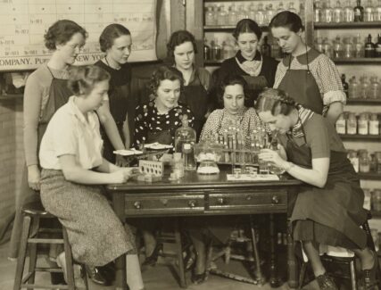 group of women standing around a lab table with periodic table in background