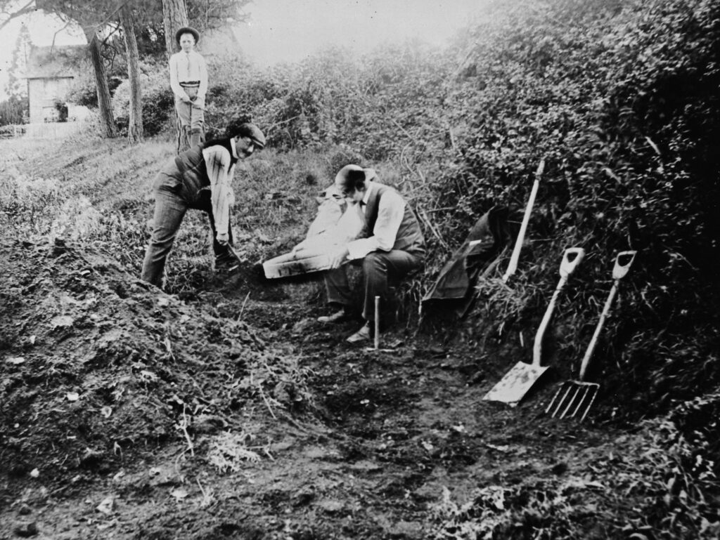 Grainy black and white photo of three men at an archaeological site