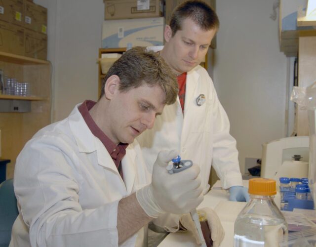 Two scientists in lab coats work in lab.