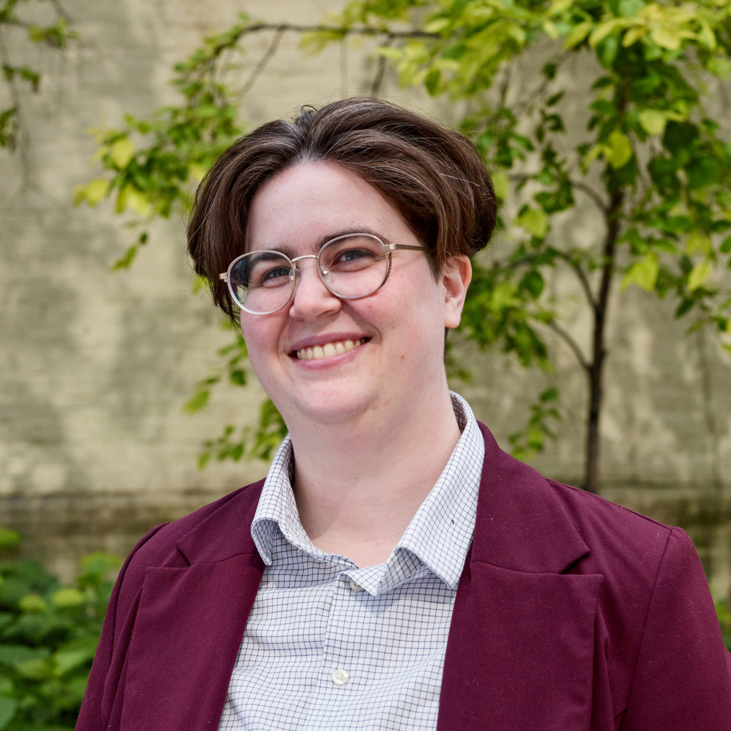 Alex outdoors, smiling, wearing glasses, checked shirt, purple blazer