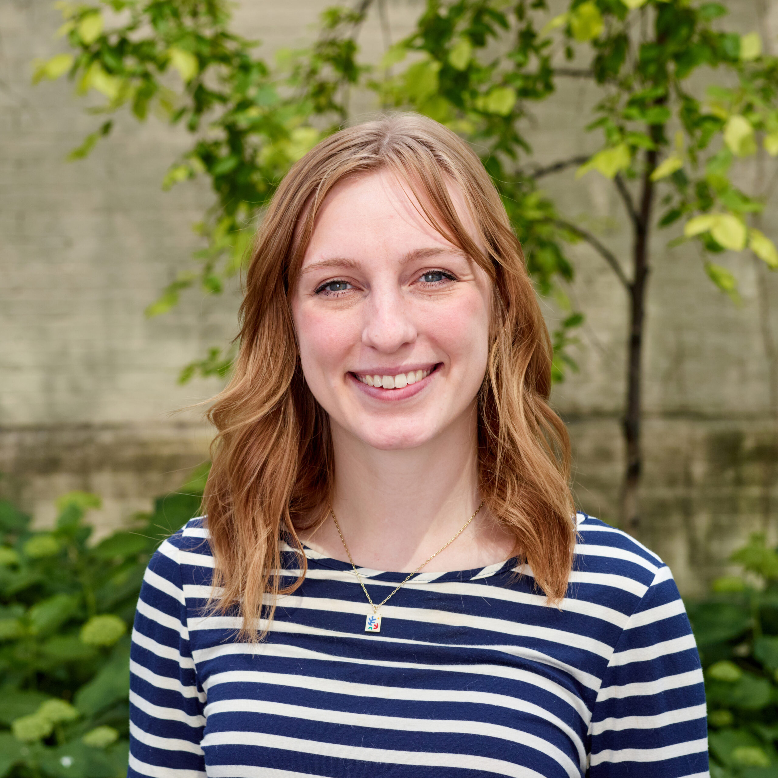 Annabel, outdoors, smiling, wearing a pendant and navy/white striped shirt