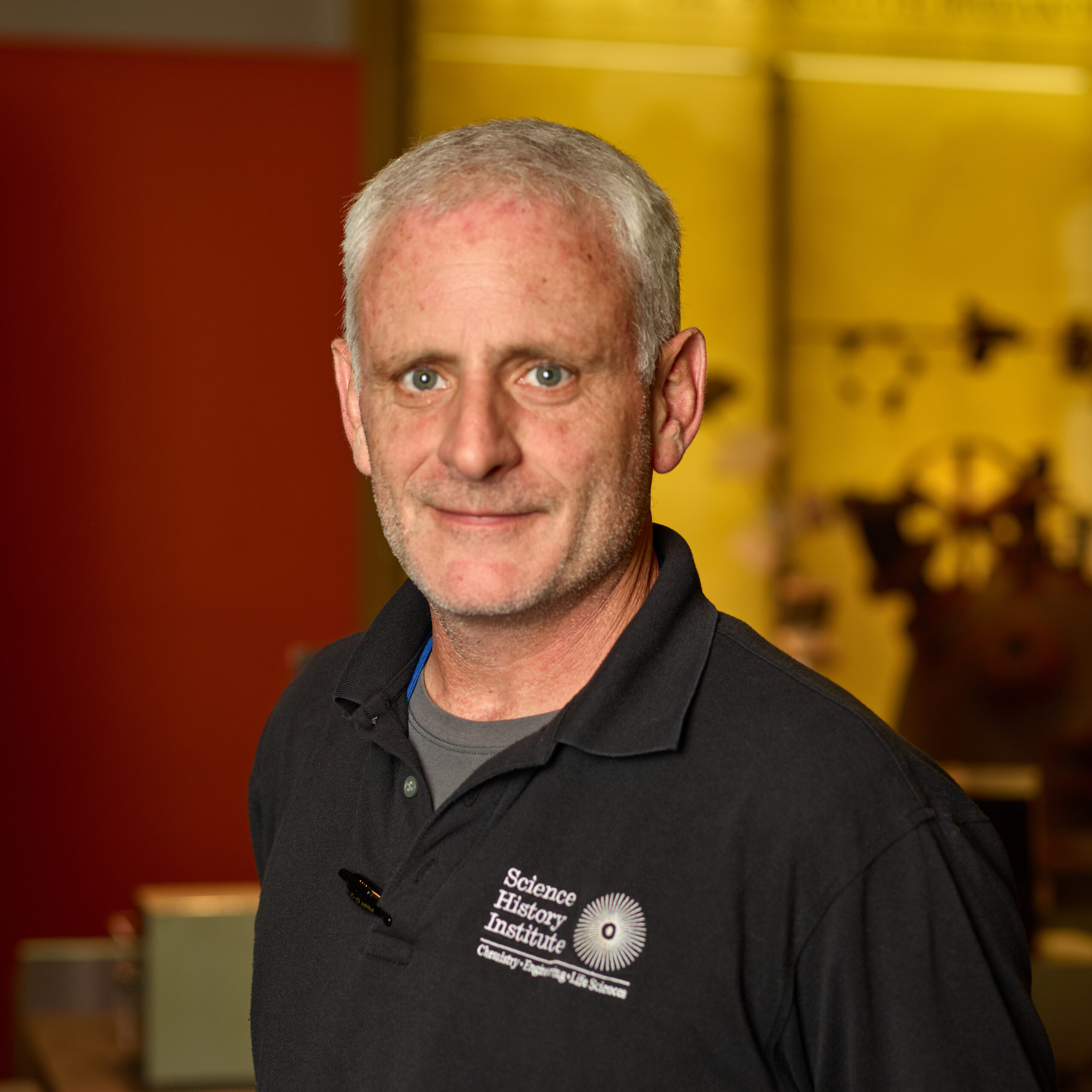 Gene in museum wearing a black collared shirt with Science History Institute logo and is smiling