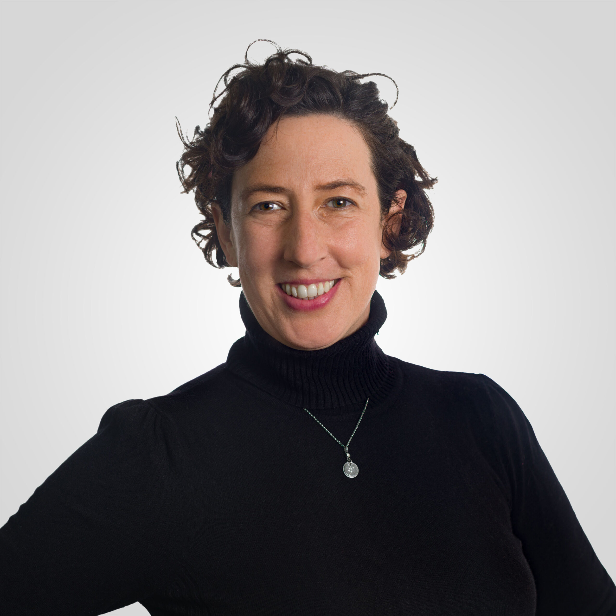 Gabriela over light gray background, smiling, wearing pendant and black turtleneck sweater