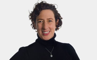 Gabriela over light gray background, smiling, wearing pendant and black turtleneck sweater