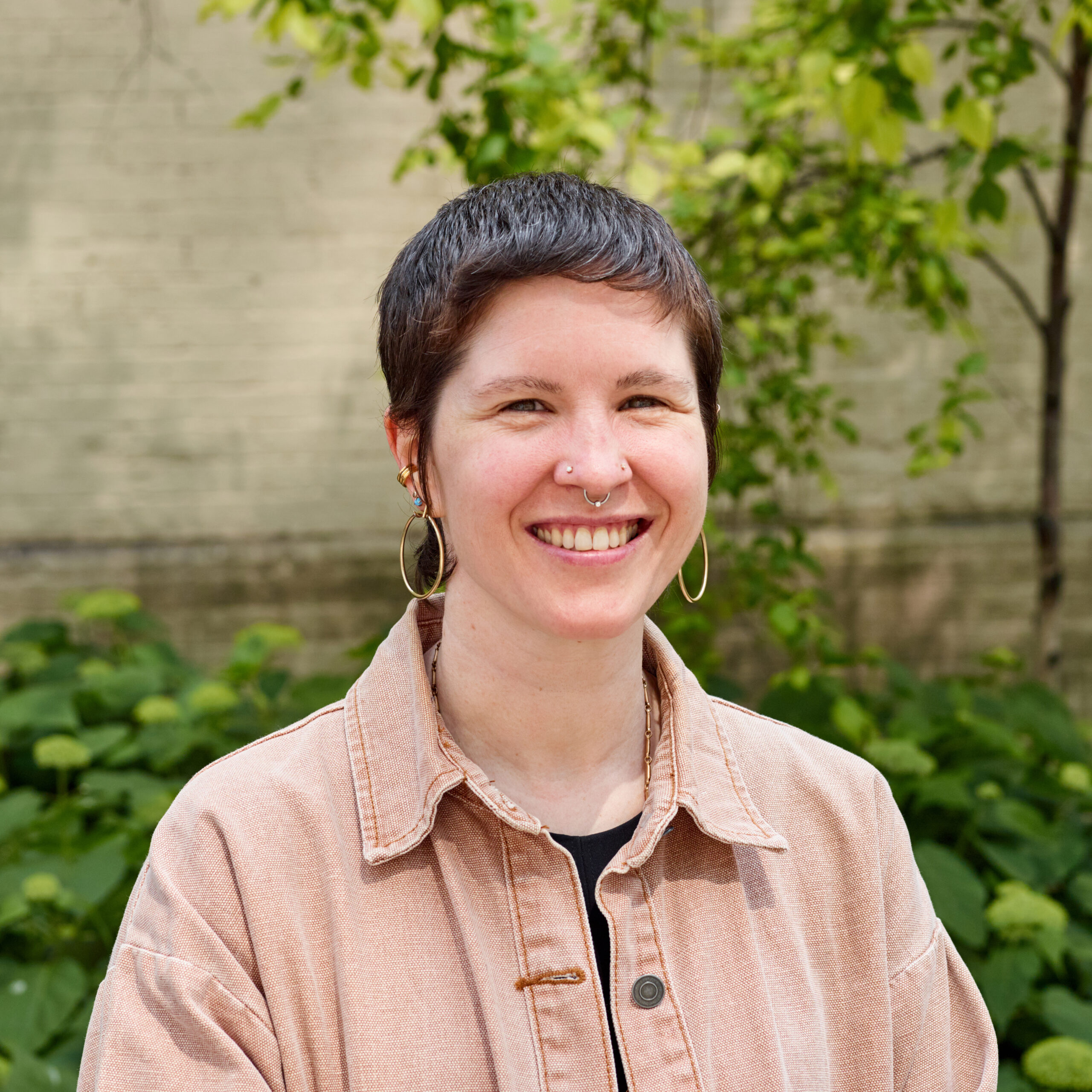 Laura, outdoors, smiling, wearing hoop earrings and coral-colored button down shirt