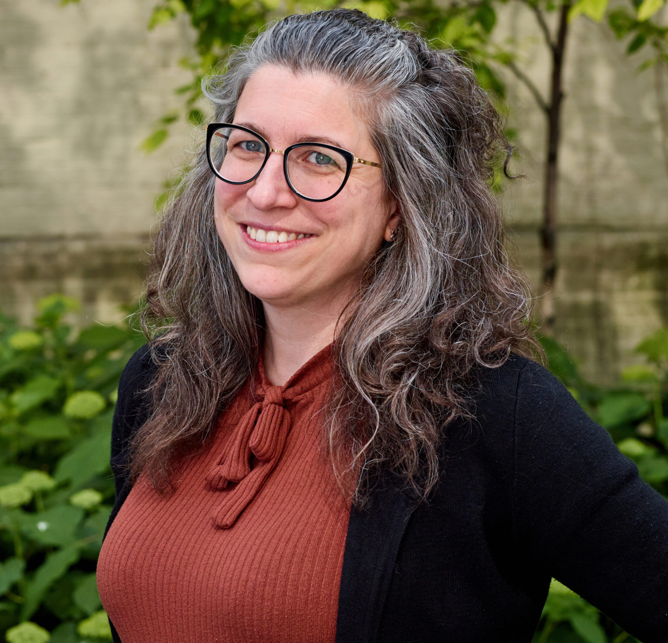 Michelle outdoors, smiling, wearing glasses and terra cotta sweater under black cardigan