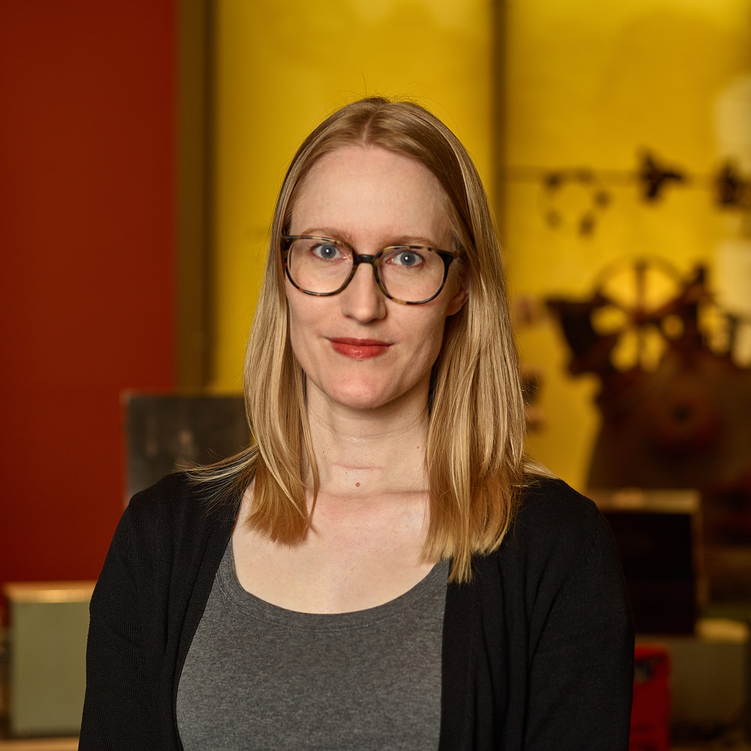 Sarah in museum wearing glasses, gray shirt, black cardigan