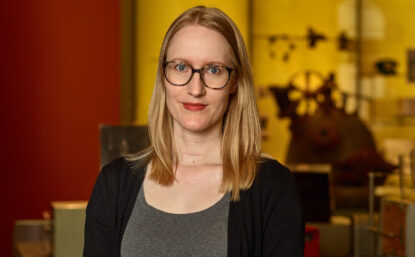 Sarah in museum wearing glasses, gray shirt, black cardigan