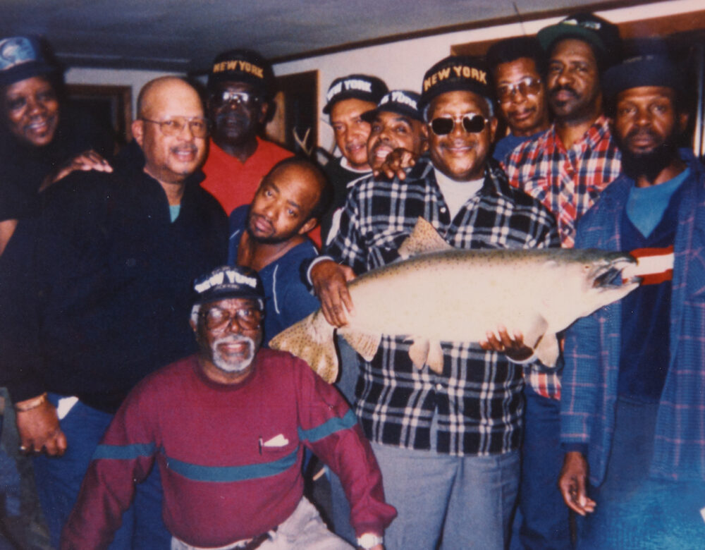 Group of eleven older men posing with a large taxidermy fish