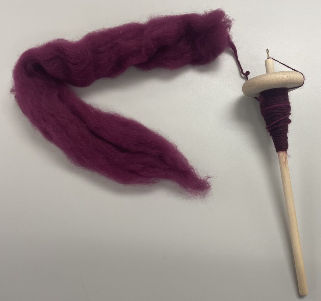 A spindle with maroon wool yarn