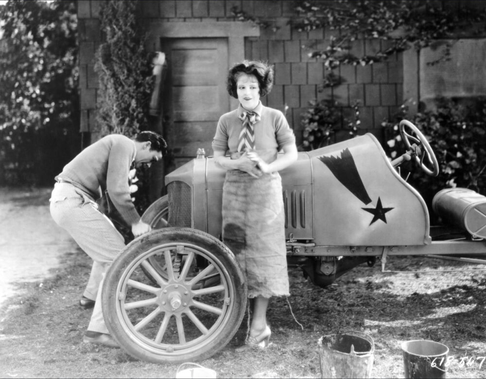 Clara Bow in front of a car being repaired