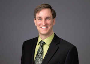 Caleb Funk smiling, wearing black blazer, green dress shirt, tie