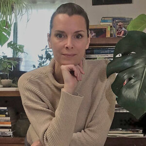 Elizabeth Shane Quinn in taupe sweater, hair pulled back, chin resting on hand