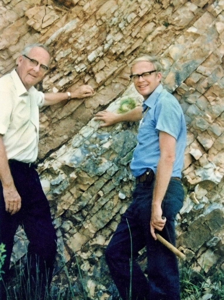 Color photo of two men in front of rock formation