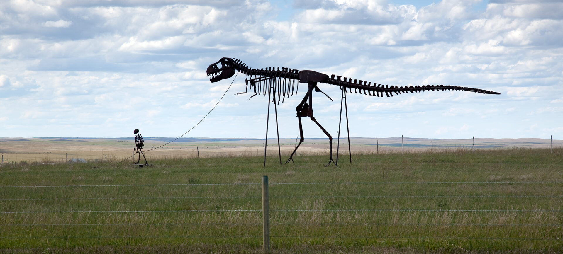 Roadside sculpture showing a skeleton man walking a skeleton dinosaur
