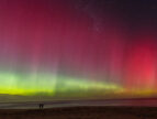 Color photograph of a vivid aurora in the sky over a beach