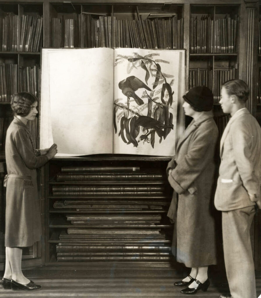 Old photograph of three people standing around a very large book opened upright