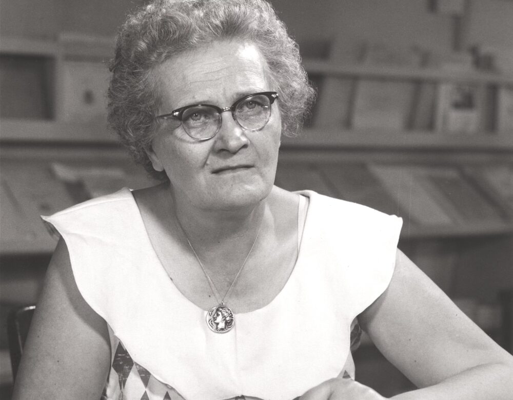 woman with glasses seated at a table reading a book