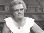 woman with glasses seated at a table reading a book
