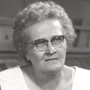 woman with glasses seated at a table reading a book