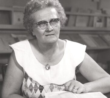woman with glasses seated at a table reading a book