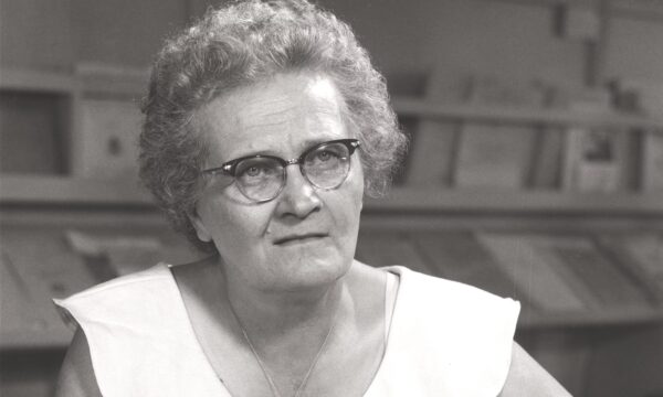 woman with glasses seated at a table reading a book
