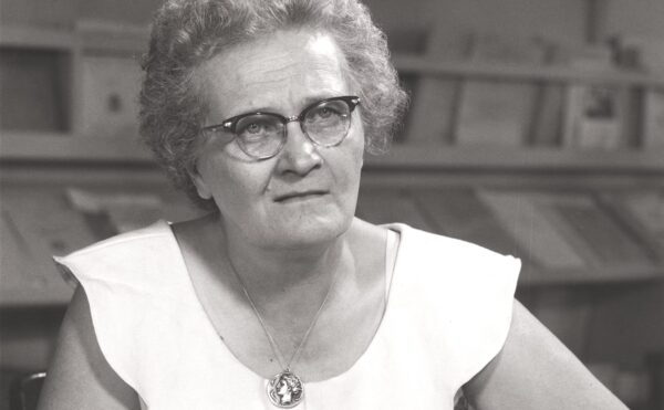 woman with glasses seated at a table reading a book