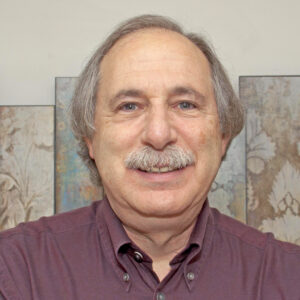 Bernard Lightman, dark red collared shirt, in front of an artwork on a wall