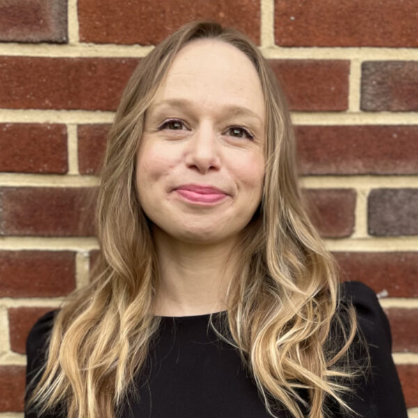 Elisabeth smiling, wearing black, in front of a brick wall